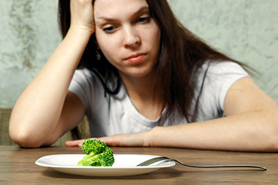 Photo of person staring at plate with a single piece of broccoli on it
