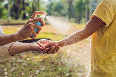 Photo of an adult spraying a young child with protective insect spray