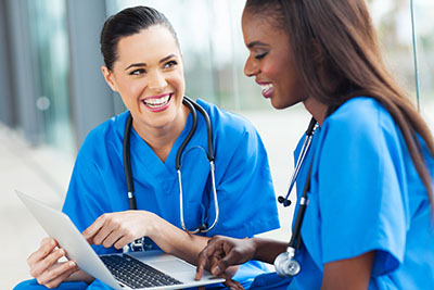 photo of nurses smiling at each other pointing to laptop