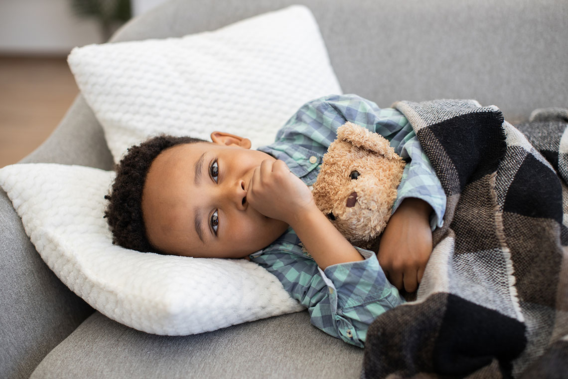 Photo of young boy lying on couch coughing